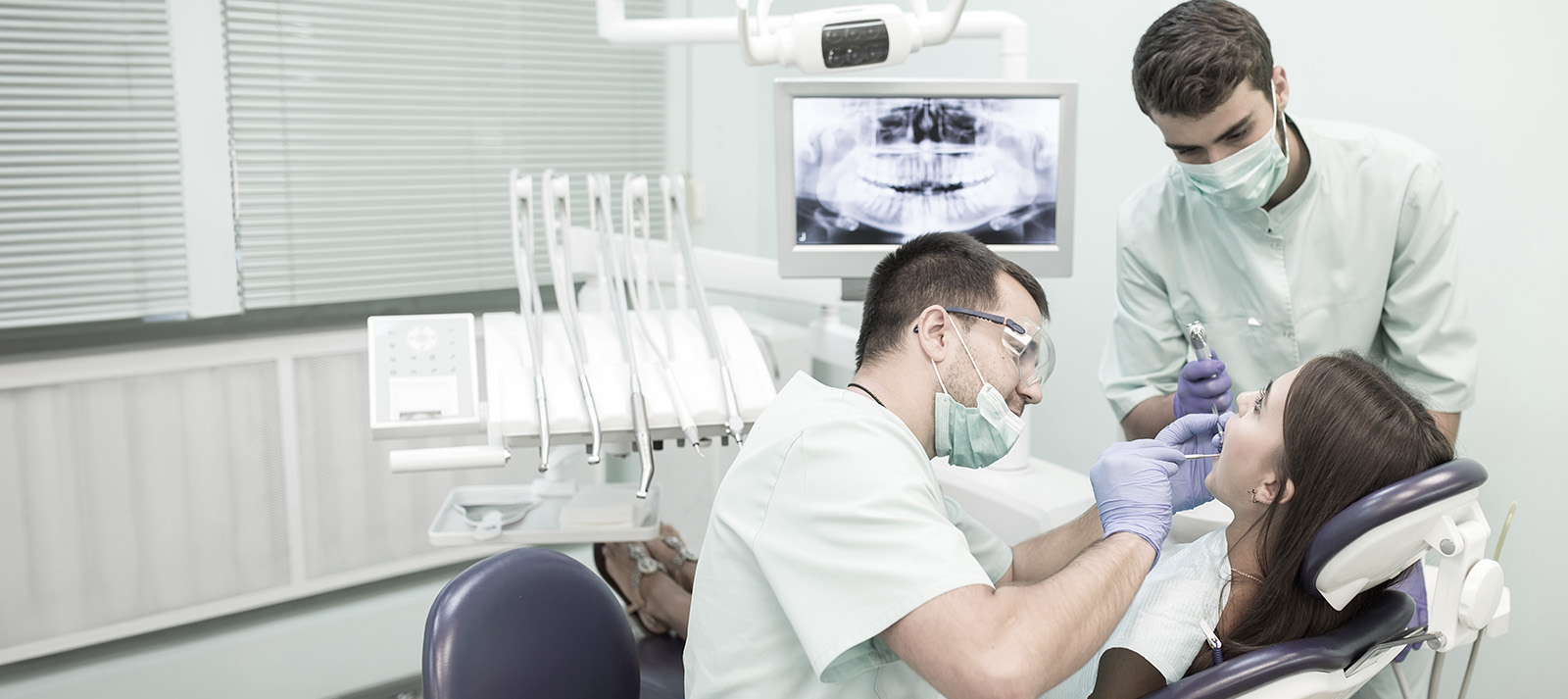 A dental office scene featuring a dentist performing an examination on a patient with two assistants attending.